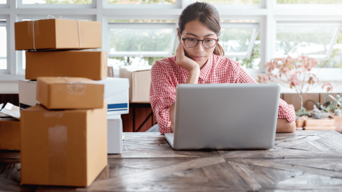 Female small business owner on a computer, sitting next to packages waiting to ship.